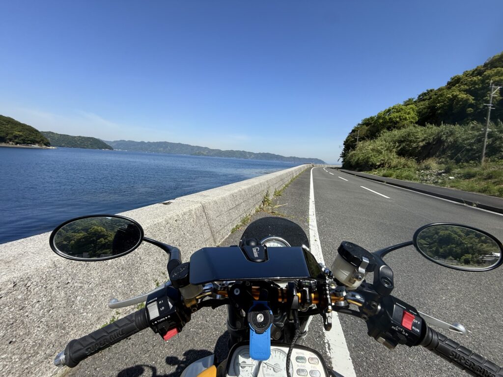 バイクのハンドル越しに撮影された青い海と青空が広がる海岸線の道路